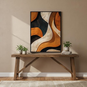 May include: Abstract art print in a black frame. The artwork features flowing, layered shapes in shades of orange, black, and white. The print is displayed on a wooden console table with small potted plants.