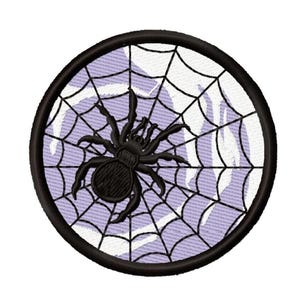 Puede incluir: Parche bordado redondo negro con un diseño de araña negra en una telaraña. La telaraña es blanca sobre un fondo lila claro. El parche tiene un borde negro, ideal para Halloween o proyectos temáticos de terror.