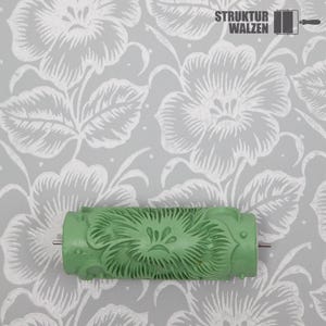 Könnte beinhalten: Eine grüne Farbwalze mit floralem Muster wird vor einem grauen und weißen floralen Tapetenhintergrund gezeigt. Die Walze hat ein detailliertes, strukturiertes Muster. Der Text "STRUKTUR WALZEN" ist oben rechts sichtbar.