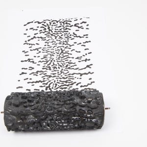 Könnte beinhalten: Eine schwarze, strukturierte Walze mit einem Metallstab ist am unteren Rand des Bildes zu sehen. Die Walze wurde verwendet, um ein Muster aus schwarzen Punkten auf einer weißen Oberfläche zu erzeugen. Das Muster ähnelt einer Reihe verbundener Punkte.