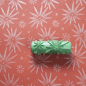 May include: A green paint roller with a starburst design. The roller is on a red background with a white starburst pattern.