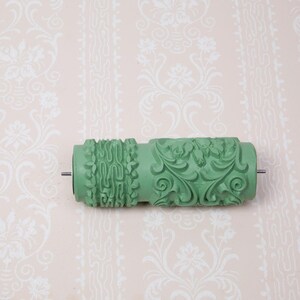 Può includere: Rullo di vernice verde con un motivo decorativo per creare pareti testurizzate. Il rullo ha un design floreale con dettagli intricati.