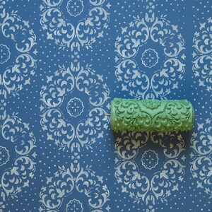 May include: A green paint roller with a decorative pattern is shown against a blue background with a white damask pattern.