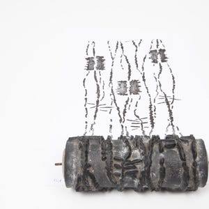May include: Abstract sculpture featuring a dark, textured cylindrical base with vertical, linear black markings above. The artwork has a minimalist aesthetic, with a focus on form and texture against a white background.