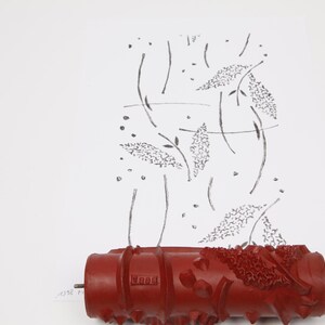 Könnte beinhalten: Eine rote Farbrolle mit strukturierter Oberfläche ist am unteren Bildrand zu sehen. Oberhalb der Rolle ist ein Muster aus schwarzen Linien und Formen zu sehen, die Blättern und Stängeln ähneln, auf weißem Hintergrund. Die Rolle ist für dekorative Muster konzipiert.