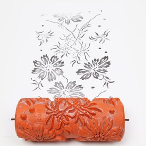 May include: Orange paint roller with a floral design. The roller is used to create a repeating pattern on a wall or other surface.