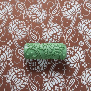 Könnte beinhalten: Eine grüne Farbrolle mit einem floralen Muster. Die Rolle liegt auf einer braunen Oberfläche mit einem weißen floralen Muster.