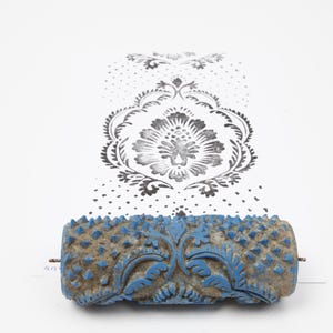 May include: A blue and brown patterned paint roller with a floral design. The roller has a textured surface and is shown rolling a floral pattern onto white paper. The printed pattern is black and white.