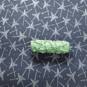 Op de afbeelding: Een groene verfroller met een sterpatroon. De roller ligt op een donkerblauw oppervlak met een wit sterpatroon.
