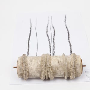 May include: A cylindrical patterned roller tool with a textured, off-white surface and raised ridges. The roller is positioned on a white sheet of paper featuring three vertical black lines, with the number 1060 and other handwritten text visible.
