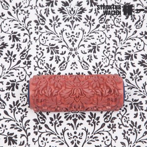 May include: A cylindrical rubber paint roller featuring a raised, intricate floral damask pattern in a terracotta color. The roller is positioned over a white surface printed with a matching black damask design. The text STRUKTUR WALZEN is visible.