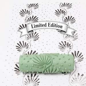 Könnte beinhalten: Eine mintgrüne Musterwalze mit floralem Design und dem Schriftzug "Limited Edition" auf einem Banner. Die Walze ist von einem sich wiederholenden Muster aus stilisierten Blumen und Punkten auf weißem Hintergrund umgeben.