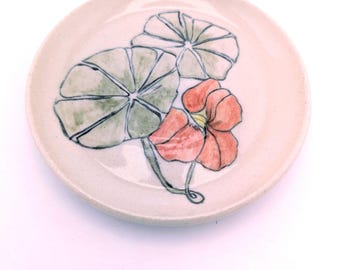 May include: A small, white ceramic plate with a hand-painted design of green leaves and a red flower. The plate is perfect for serving small snacks or desserts.