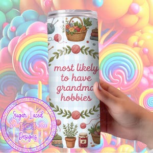 K&ouml;nnte beinhalten: Ein Edelstahlbecher mit hellblauem Vichy-Muster und dem Text "most likely to have grandma hobbies". Das Design umfasst Illustrationen von Garn, Stricknadeln, Pflanzen, B&uuml;chern und einem Blumenkorb. Der Becher wird von einer Person gehalten.