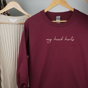 Puede incluir: Sudadera color burdeos con el texto "my head hurts" en letra blanca.