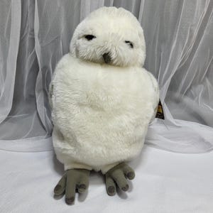 Op de afbeelding: Een zacht, wit uilenspeelgoed met een zachte, donzige textuur. De uil heeft donkere ogen, een grijze snavel en grijze poten. Het speelgoed is ontworpen om op een sneeuwuil te lijken en is geschikt voor kinderen.