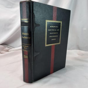 Könnte beinhalten: Ein gebundenes Buch mit dem Titel "Electric Machinery" von McGraw-Hill. Das Buch hat einen schwarzen Einband mit roten vertikalen Streifen und goldfarbenen Buchstaben. Der Einband trägt auch den Text "Electrical and Electronic Engineering Series". Es ist eine zweite Auflage.