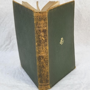 May include: A hardcover book titled Roman History with a dark green textured cover and a worn, gold-toned spine. The front cover features a gold embossed monogram logo. The spine displays the title and the publisher name Heinemann in gold text.