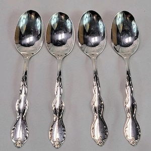 Może przedstawiać: Cztery srebrne łyżki z ozdobnymi uchwytami i owalnymi miseczkami. Łyżki odbijają otoczenie, prezentując klasyczny design sztućców.