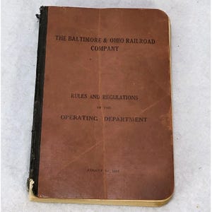 May include: A vintage booklet with a brown cover, featuring the text "THE BALTIMORE & OHIO RAILROAD COMPANY" and "RULES AND REGULATIONS OF THE OPERATING DEPARTMENT". The date "AUGUST 1912" is also visible. The booklet has a black spine.