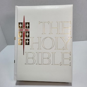 Könnte beinhalten: Weißes, ledergebundenes Buch mit goldener Aufschrift "THE HOLY BIBLE". Auf dem Einband befindet sich ein rotes und goldenes Sternendesign.