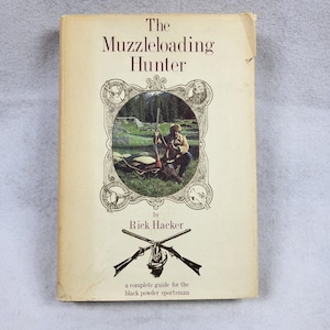 Puede incluir: Libro antiguo titulado "The Muzzleloading Hunter" de Rick Hacker. La portada presenta un cazador con un rifle y un ciervo, rodeados de elementos decorativos. El libro es una guía completa para el deportista de pólvora negra.