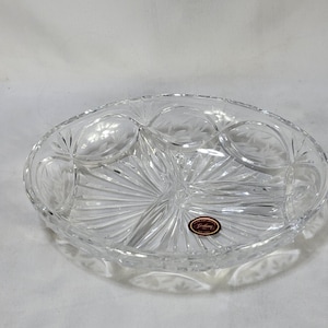 May include: A clear, oval-shaped crystal serving dish featuring a divided interior with three distinct sections. The glass is decorated with intricate, hand-cut radial patterns and floral etchings. A small, oval-shaped sticker reads Hand Cut Crystal Gorham Poland.