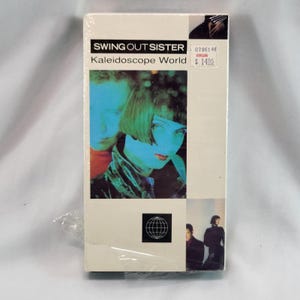May include: A sealed VHS tape of the album "Kaleidoscope World" by Swing Out Sister. The cover features a photo of two people with blue-toned skin and green hair. The band's name and album title are printed in black.