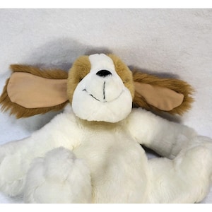 May include: A plush dog toy with a white body, tan ears, and a brown head. The dog has a black nose and a smiling mouth. The toy is soft and cuddly, perfect for children.