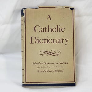 May include: A hardcover book titled A Catholic Dictionary, edited by Donald Attwater, Second Edition, Revised. The cover is tan with dark brown text and a decorative flourish. The book shows signs of wear along the top edges and spine.