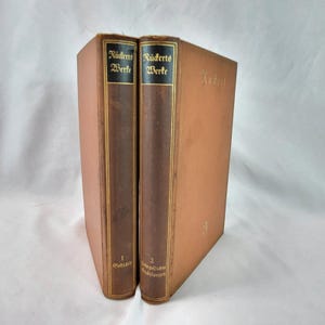 Pode incluir: Dois livros antigos com capas castanhas e bege. As lombadas são castanhas escuras com letras douradas que dizem "Rückerts Werke". O primeiro livro está rotulado como "1 Gedichte", e o segundo como "2 Lehrgedichte Erzählungen".