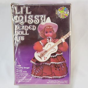May include: A Li'l Missy Beaded Doll Kit in a rectangular box. The packaging features a graphic of a doll wearing a white hat and a red dress, holding a white guitar. Text on the box includes 'Li'l Missy Beaded Doll Kit' and 'Country Singer'.