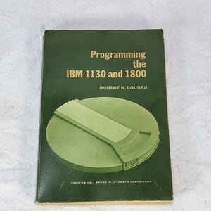 Puede incluir: Un libro verde titulado Programming the IBM 1130 and 1800 de Robert K. Louden. La portada presenta un gráfico verde claro de una unidad de almacenamiento en disco con el logo de IBM. El texto en la parte inferior dice Prentice-Hall Series in Automatic Computation.