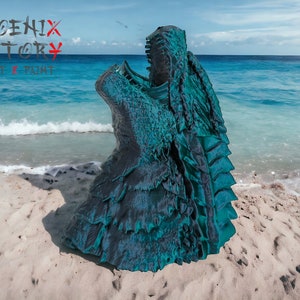 May include: A teal and black 3D printed sculpture of a dragon's head with its mouth open, on a sandy beach with blue water in the background. The sculpture is labelled "PHOENIX FACTORY PRINT & PAINT".