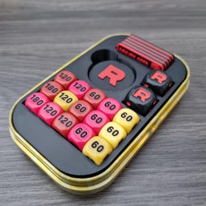 May include: A black and yellow game case featuring a red "R" logo and dice. The case contains coloured dice with numbers such as 60, 120, and 180. A separate red and black piece is also present.