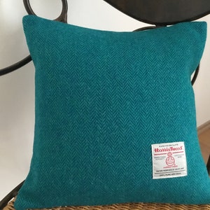 Op de afbeelding: Tealblauwe kussenhoes met een herringbone patroon en een "Harris Tweed" label.