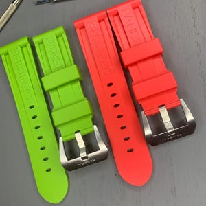 Puede incluir: Correas de reloj verde brillante y rojo coral con hebillas plateadas, con la marca "PANERAI" y el texto "OFFICINE". También se ven dos herramientas de reparación de relojes.