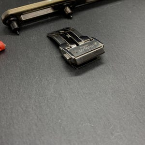 May include: A silver watch clasp with the brand name "Hublot Geneve" engraved. A red tool and a watch repair tool are also visible. The items are on a dark grey surface.