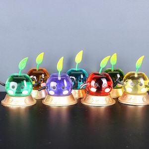 May include: A set of seven colourful, glass figurines with a green stem and a face. Each figurine is sitting on a gold base.