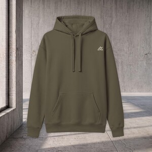 Puede incluir: Una sudadera con capucha de color verde oliva que presenta un pequeño logotipo blanco de una cordillera en el pecho izquierdo. La sudadera incluye un bolsillo tipo canguro, mangas largas con puños acanalados, cordón y dobladillo acanalado.