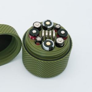 May include: A green cylindrical container with a lid, filled with various sized batteries. The container has a textured diamond pattern.