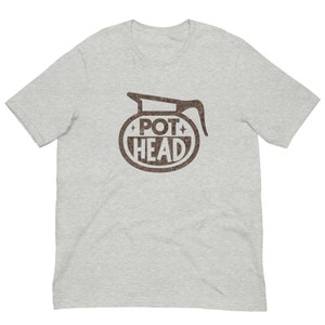 May include: A gray t-shirt with a brown graphic of a coffee pot with the text "POT HEAD" inside a circle.