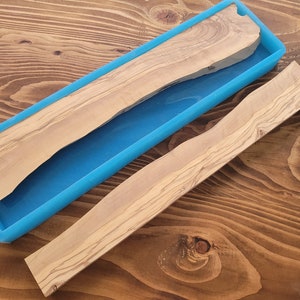 May include: A light-colored wooden slab and a curved wooden piece sit next to a rectangular, bright blue container. The wood has a natural grain pattern. The container is empty. The items are on a wooden surface.