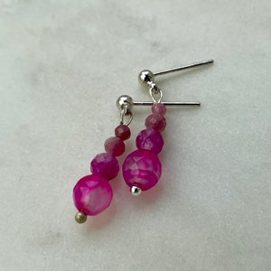 Pode incluir: Um par de brincos de pedra preciosa rosa com postes e contas prateadas. Os brincos apresentam um degradê de tons de rosa.