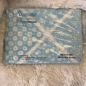 May include: A packaged king fitted sheet with a blue and white floral pattern. The packaging reads "Wamsutta Ultracale" and "No Ironing Necessary." The sheet is designed for a 78 x 80 inch mattress.