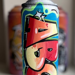 May include: A spray paint can with a blue, green, and white background. The can is painted with the word "ABS" in red, yellow, and white.