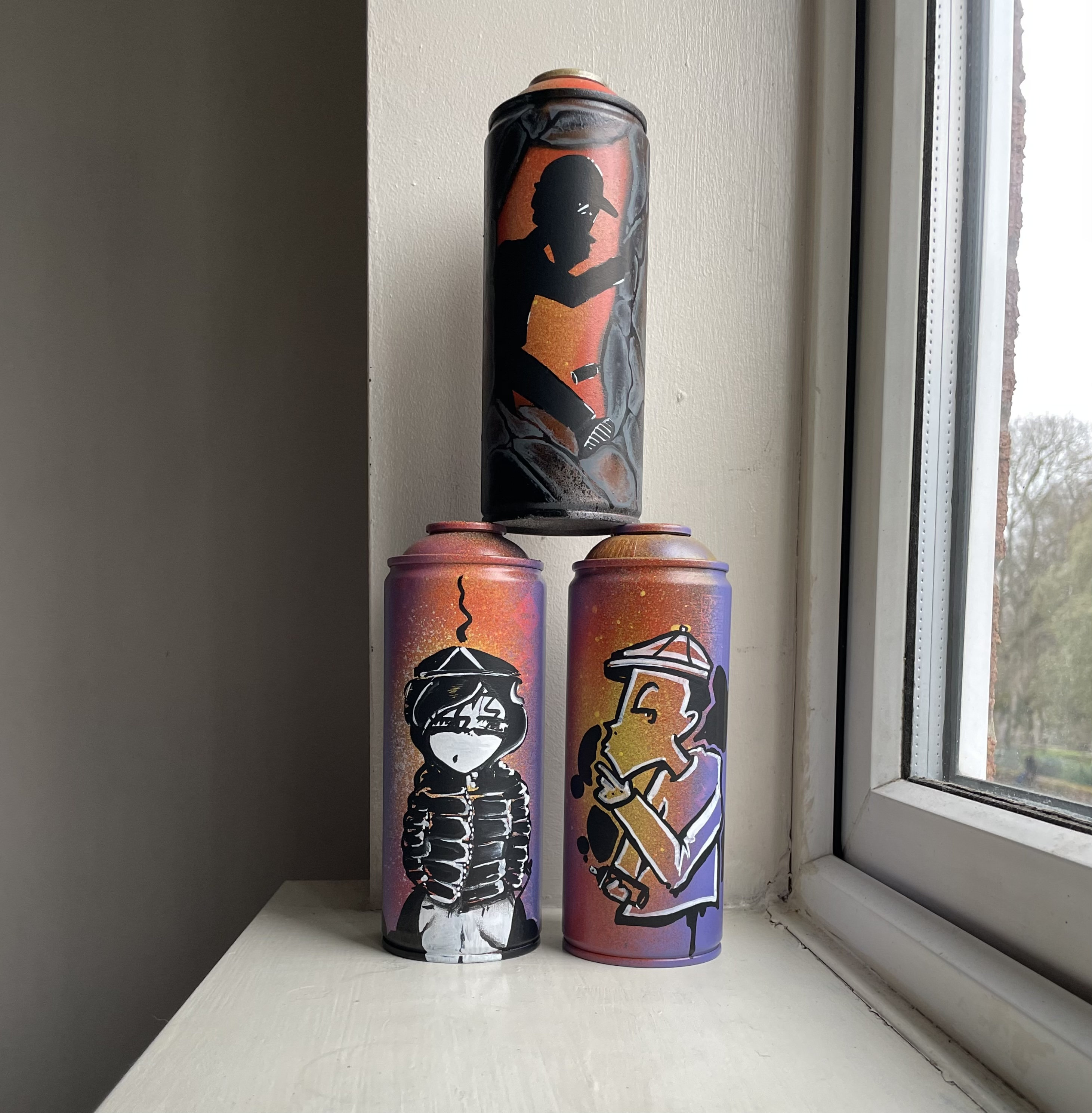 Custom spray paint cans with graffiti art on a windowsill