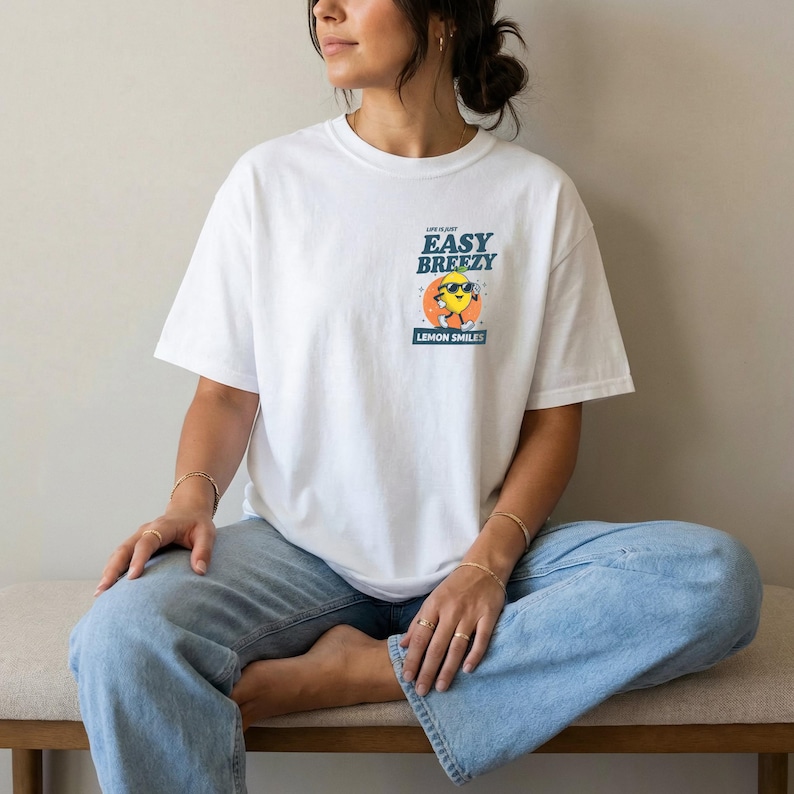 May include: White t-shirt with a graphic of a smiling lemon wearing sunglasses, the text "Easy Breezy Lemon Smiles" is above the lemon. The shirt is a short-sleeved, casual style.