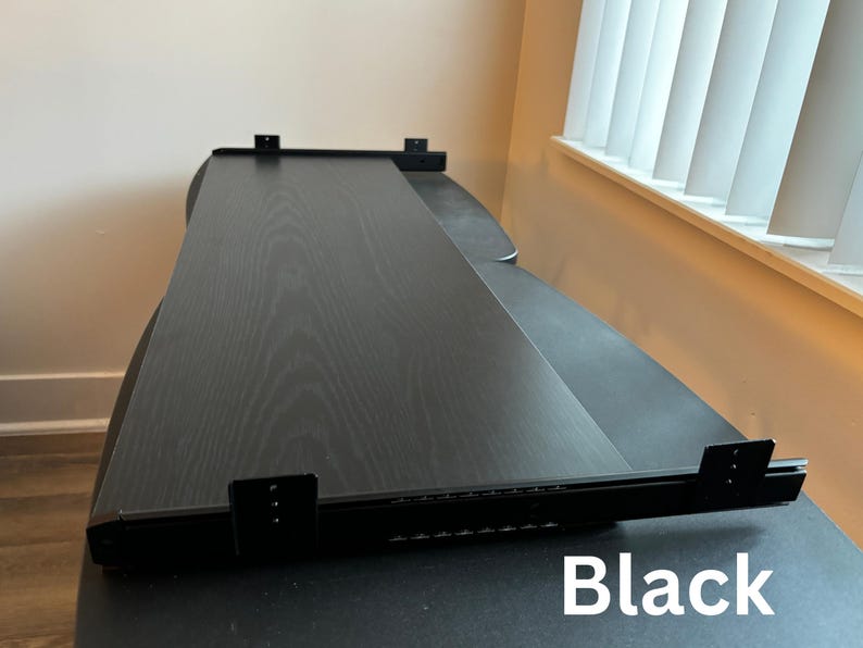 Puede incluir: Escritorio negro con acabado de vetas de madera. El escritorio tiene una superficie larga y rectangular con un soporte de metal negro. La palabra "Black" est&aacute; impresa en blanco en la esquina inferior derecha.