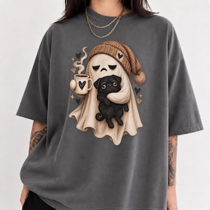 May include: A charcoal grey short-sleeve t-shirt featuring a graphic print of a beige ghost wearing a brown knit beanie, holding a steaming mug with a heart design, and embracing a small black pug dog surrounded by small heart and star icons.